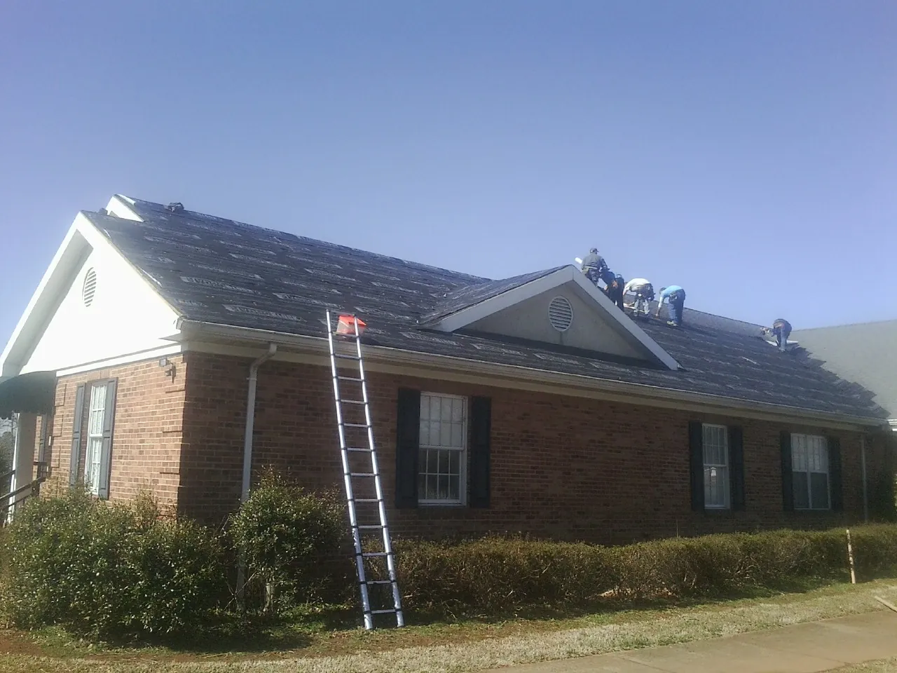 Crew tearing shingles off a brick ranch roof with a ladder set — Emergency Roof Repair work by our crew in Bloomfield