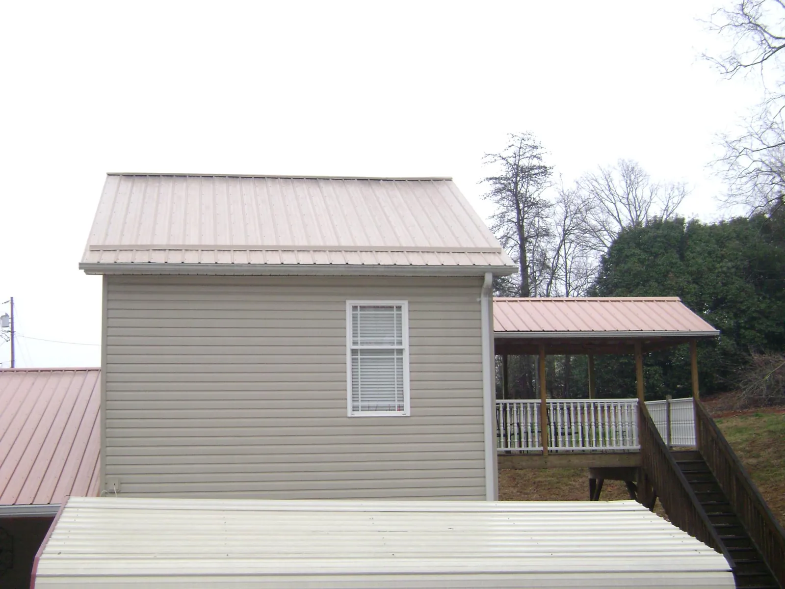 Tan metal roofs on a two story addition and attached porch, from a Roof Replacement job in Bloomfield